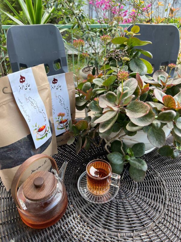 بسته چای هرمز کنار قوری شیشه‌ای و استکان در بالکن
