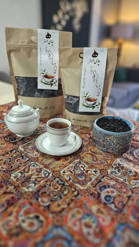 بسته‌های چای هرمز کنار قوری و فنجان روی رومیزی سنتی